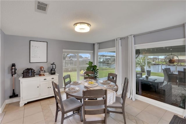 dining space featuring a textured ceiling, light tile patterned floors, visible vents, and baseboards