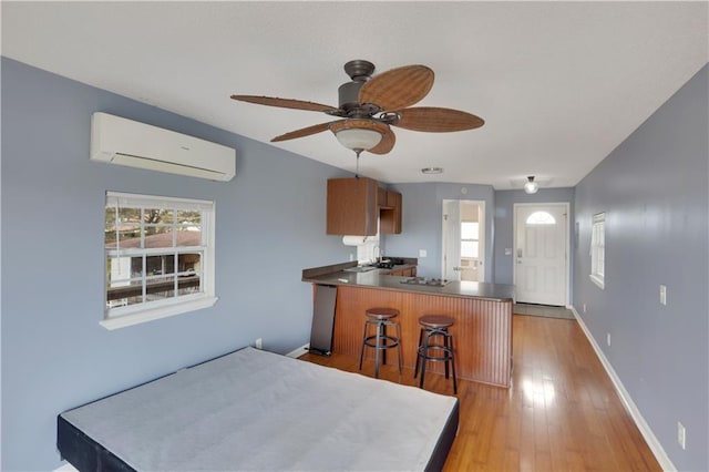 kitchen with baseboards, a breakfast bar area, a peninsula, an AC wall unit, and light wood-type flooring