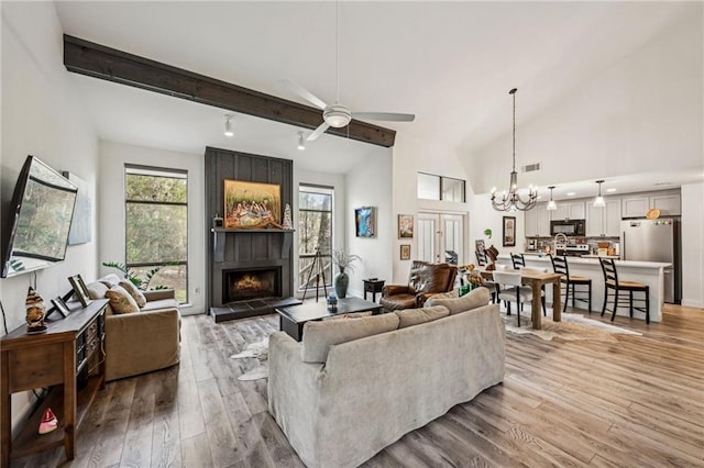 living room featuring visible vents, beamed ceiling, a tiled fireplace, and light wood-style flooring