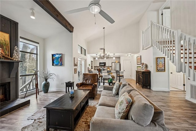 living area with beam ceiling, stairway, a tiled fireplace, and wood finished floors