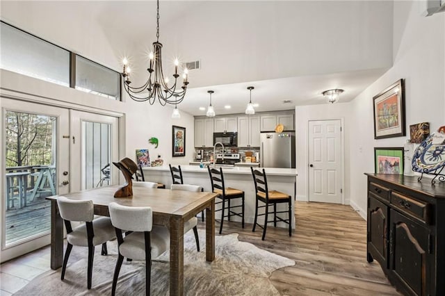 dining area featuring light wood finished floors, a towering ceiling, visible vents, and an inviting chandelier