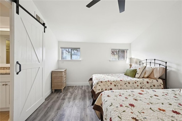 bedroom featuring a barn door, baseboards, a ceiling fan, ensuite bath, and wood finished floors