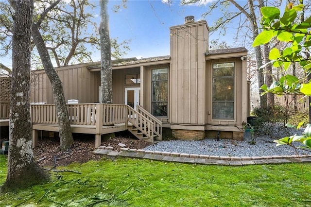 back of property featuring a chimney, a deck, board and batten siding, and a yard