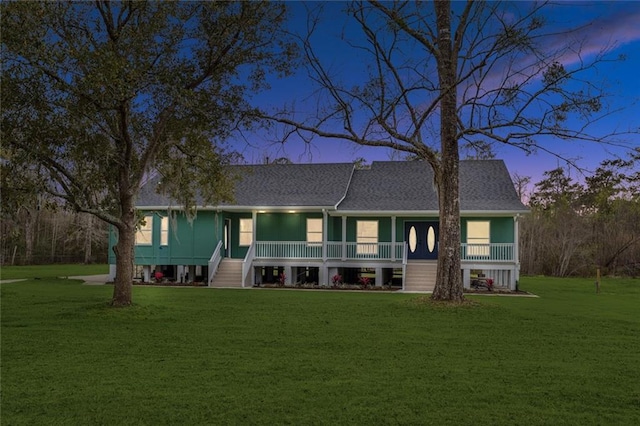 view of front of home with covered porch, a yard, and roof with shingles