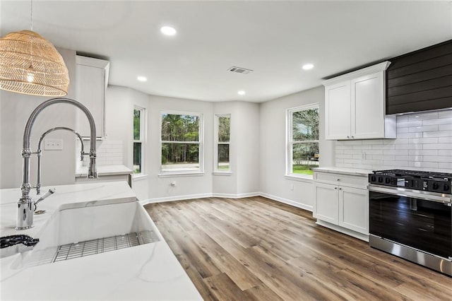 kitchen with visible vents, light stone counters, wood finished floors, gas range oven, and backsplash