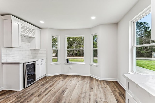 interior space featuring beverage cooler, white cabinets, decorative backsplash, light countertops, and light wood-style floors