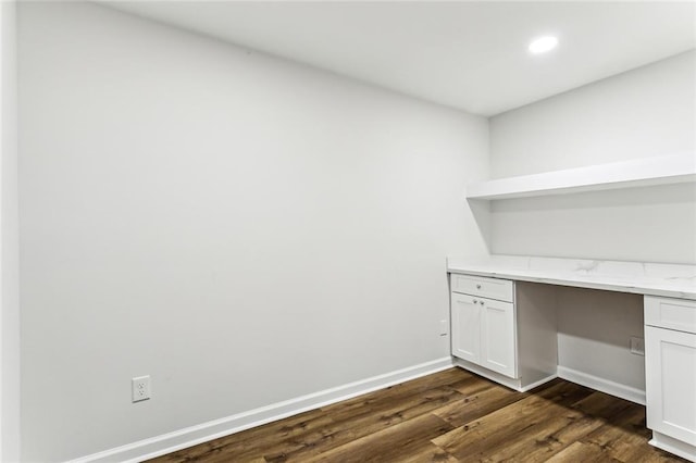 unfurnished office with built in desk, dark wood-type flooring, recessed lighting, and baseboards