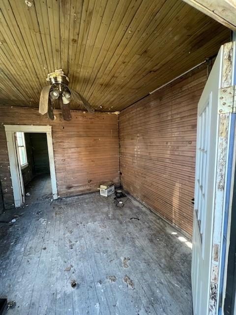 interior space featuring a ceiling fan, wooden ceiling, wood walls, and hardwood / wood-style floors