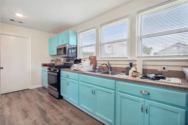 kitchen with blue cabinets, stainless steel appliances, dark wood-type flooring, a sink, and visible vents