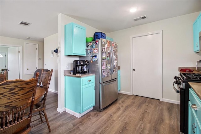 kitchen with freestanding refrigerator, range with gas cooktop, visible vents, and blue cabinetry