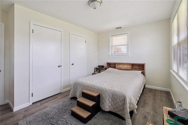 bedroom featuring baseboards, multiple windows, visible vents, and wood finished floors