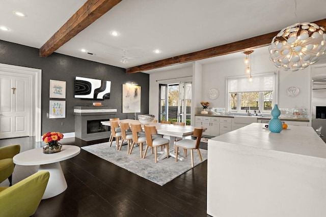 dining room with recessed lighting, dark wood-type flooring, a glass covered fireplace, beamed ceiling, and a chandelier