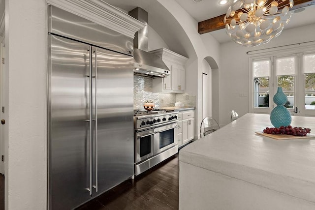 kitchen with arched walkways, decorative backsplash, white cabinetry, beamed ceiling, and high quality appliances