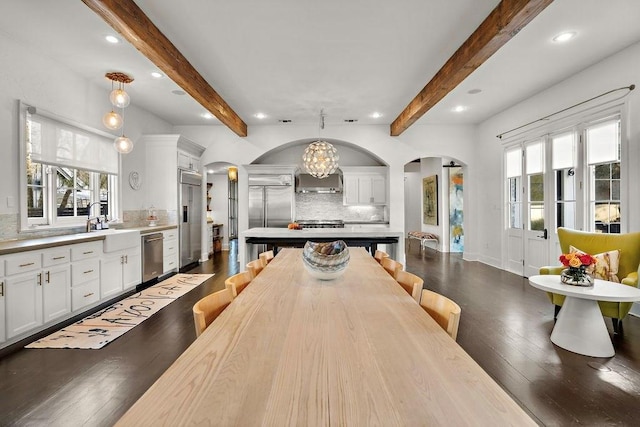 interior space with arched walkways, beamed ceiling, a healthy amount of sunlight, and dark wood-style floors