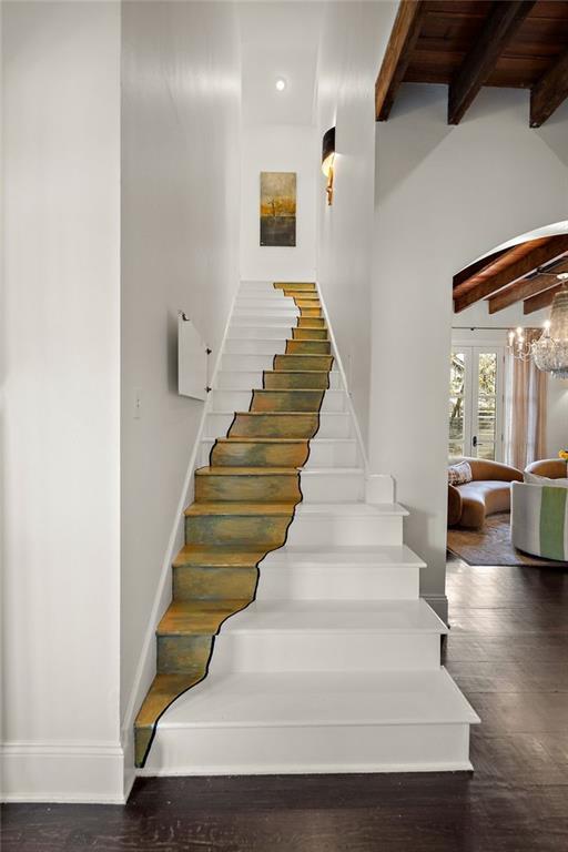 stairway with wood finished floors, baseboards, an inviting chandelier, french doors, and beamed ceiling