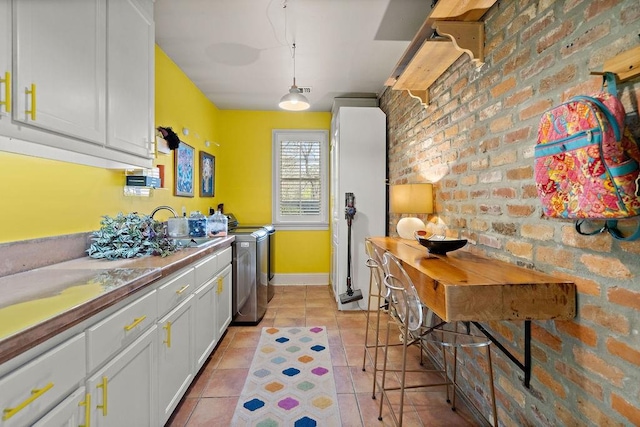 kitchen featuring brick wall, white cabinets, light tile patterned floors, baseboards, and hanging light fixtures