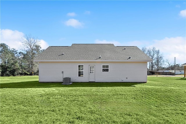 rear view of house with a shingled roof, central AC, and a lawn