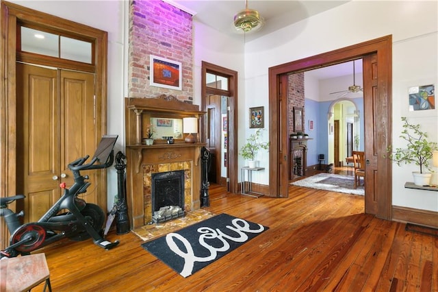 foyer with a large fireplace, ceiling fan, arched walkways, and hardwood / wood-style flooring