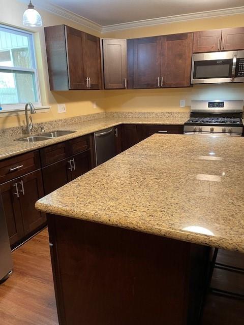 kitchen with light stone counters, crown molding, stainless steel appliances, light wood-style flooring, and a sink