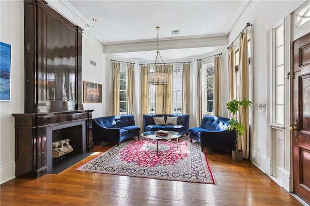 living area featuring hardwood / wood-style flooring, a large fireplace, crown molding, visible vents, and an inviting chandelier