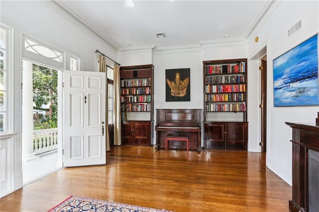 living area with crown molding, visible vents, and wood finished floors