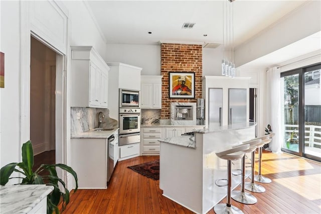 kitchen with built in appliances, a sink, visible vents, backsplash, and a warming drawer