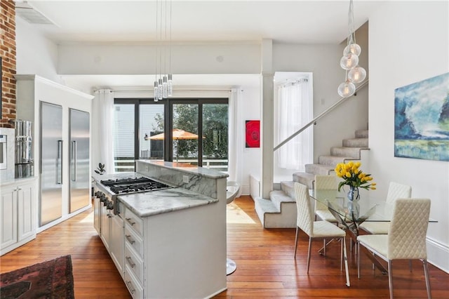 kitchen with light wood finished floors, white cabinets, a center island, stainless steel appliances, and pendant lighting