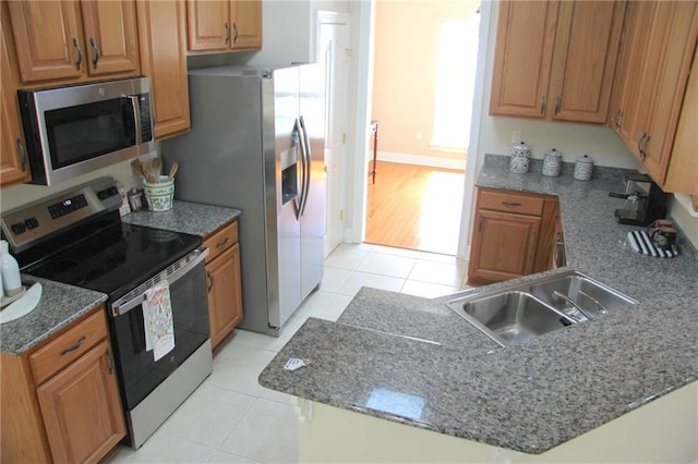 kitchen with light tile patterned floors, a peninsula, stainless steel appliances, stone counters, and a sink