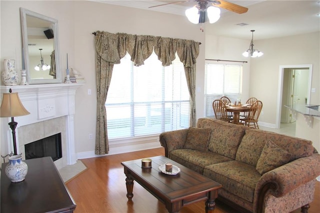 living room featuring baseboards, visible vents, wood finished floors, a fireplace, and ceiling fan with notable chandelier