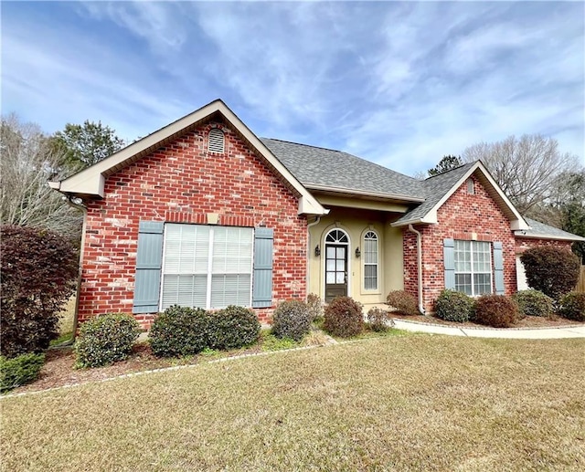 ranch-style home with a front lawn, a shingled roof, brick siding, and stucco siding