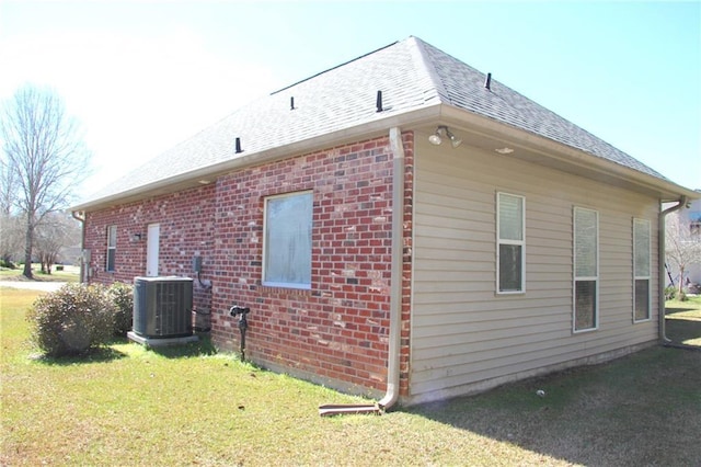 view of side of home with brick siding, a shingled roof, central AC unit, and a yard