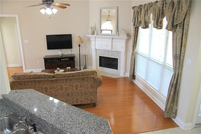 living area featuring baseboards, a fireplace, a ceiling fan, and wood finished floors