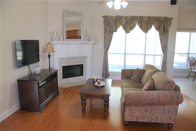 living area with a ceiling fan, a tile fireplace, baseboards, and wood finished floors