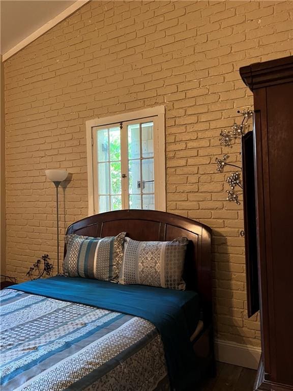 bedroom with vaulted ceiling, brick wall, wood finished floors, and baseboards