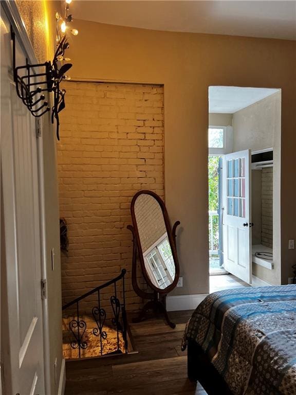 bedroom featuring brick wall, wood finished floors, and baseboards