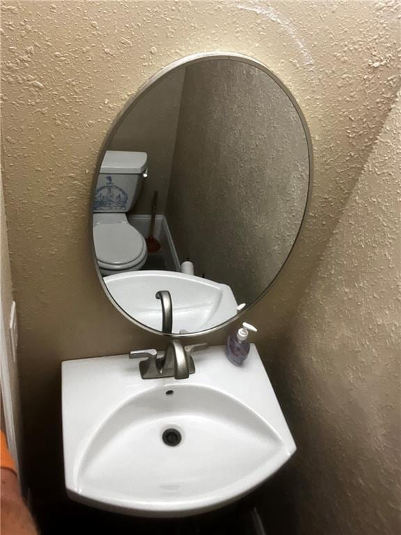 bathroom featuring a textured wall, a sink, and toilet