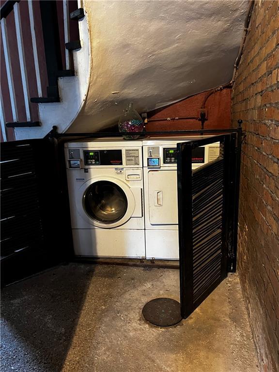 shared laundry area featuring a textured ceiling, brick wall, and washer and dryer