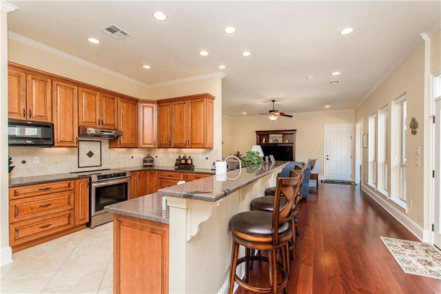 kitchen with brown cabinets, stainless steel range with electric cooktop, a peninsula, black microwave, and under cabinet range hood