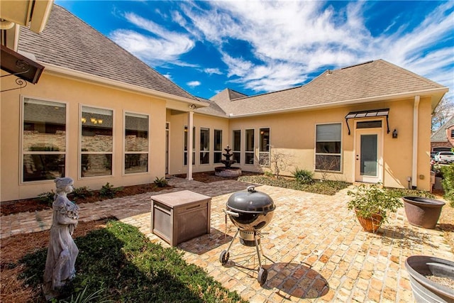 rear view of property featuring stucco siding, roof with shingles, and a patio