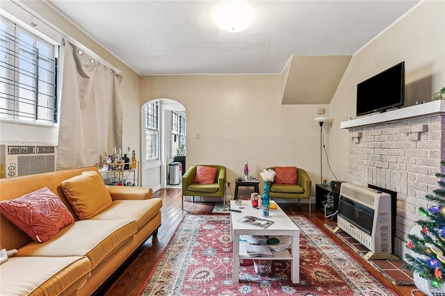 living room with baseboards, arched walkways, a glass covered fireplace, hardwood / wood-style floors, and heating unit