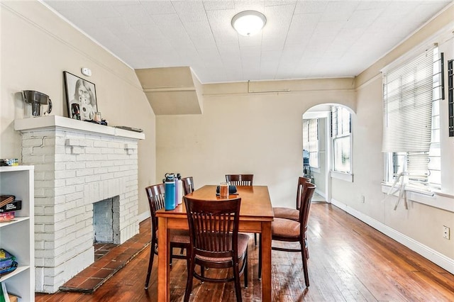 dining room with arched walkways, a fireplace, baseboards, and hardwood / wood-style flooring