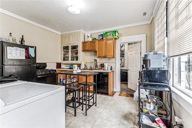 kitchen with light tile patterned floors, separate washer and dryer, black appliances, brown cabinetry, and crown molding