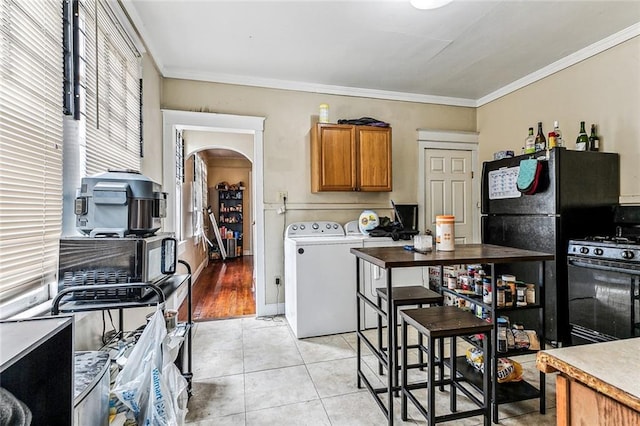 kitchen featuring arched walkways, black gas range oven, ornamental molding, brown cabinets, and washer and dryer