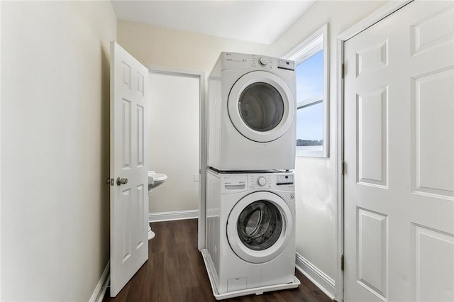 laundry area with dark wood-style floors, laundry area, stacked washer and clothes dryer, and baseboards