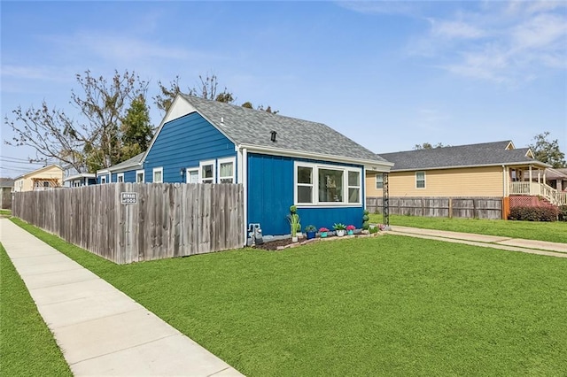 exterior space featuring a shingled roof, fence, and a lawn