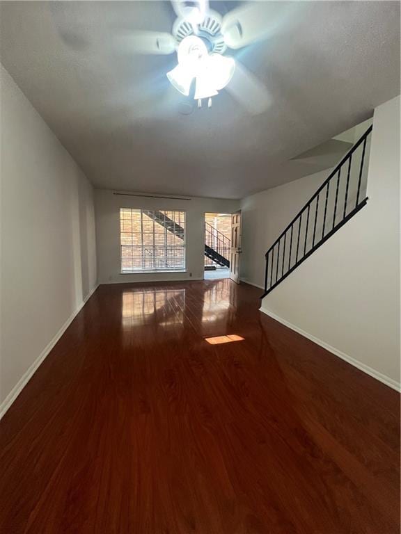 unfurnished living room with stairway, ceiling fan, baseboards, and wood finished floors