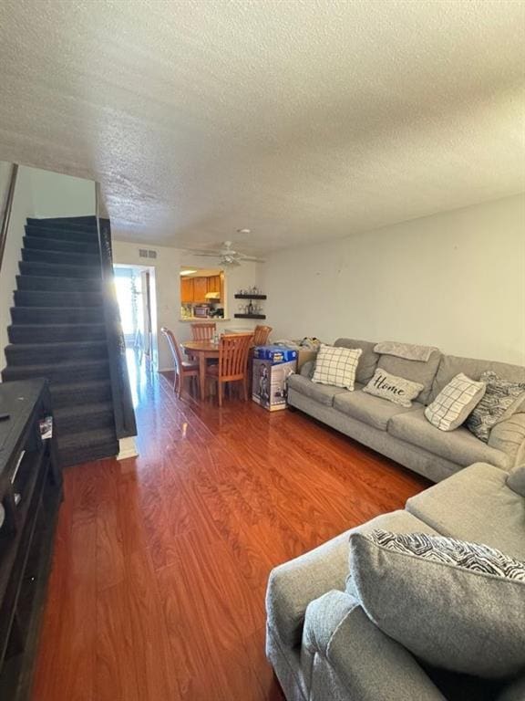 living area with a ceiling fan, stairway, wood finished floors, and a textured ceiling