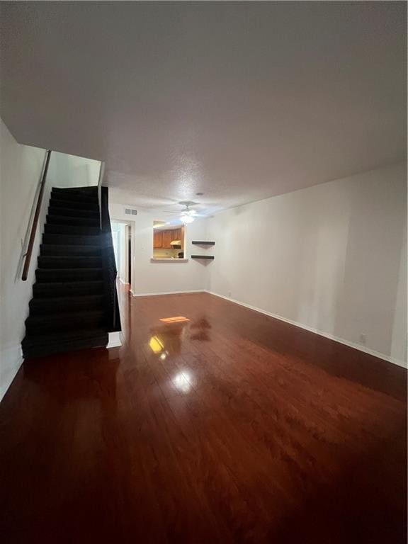 below grade area featuring ceiling fan, visible vents, dark wood finished floors, and stairs