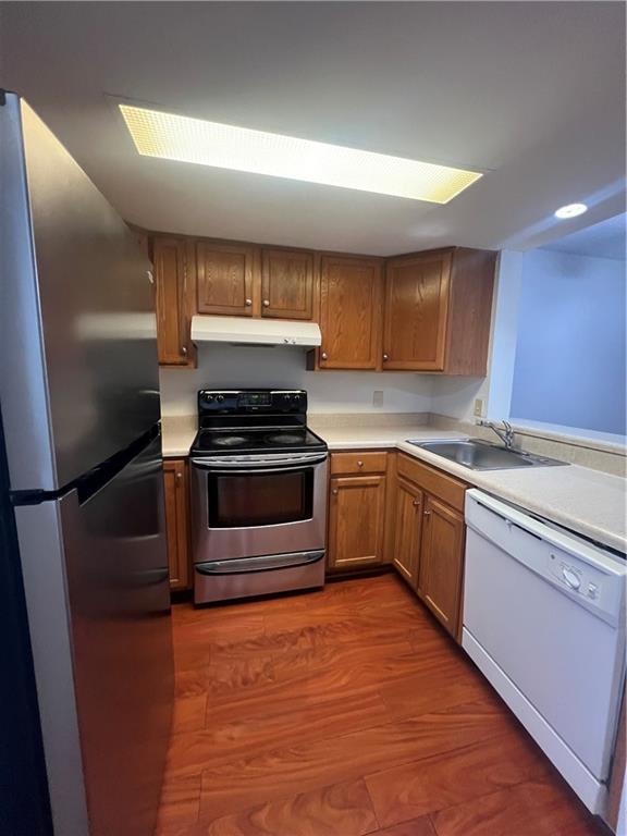 kitchen featuring dark wood-style floors, a sink, light countertops, under cabinet range hood, and appliances with stainless steel finishes