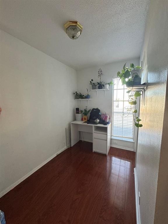 interior space with a textured ceiling, dark wood-type flooring, and baseboards